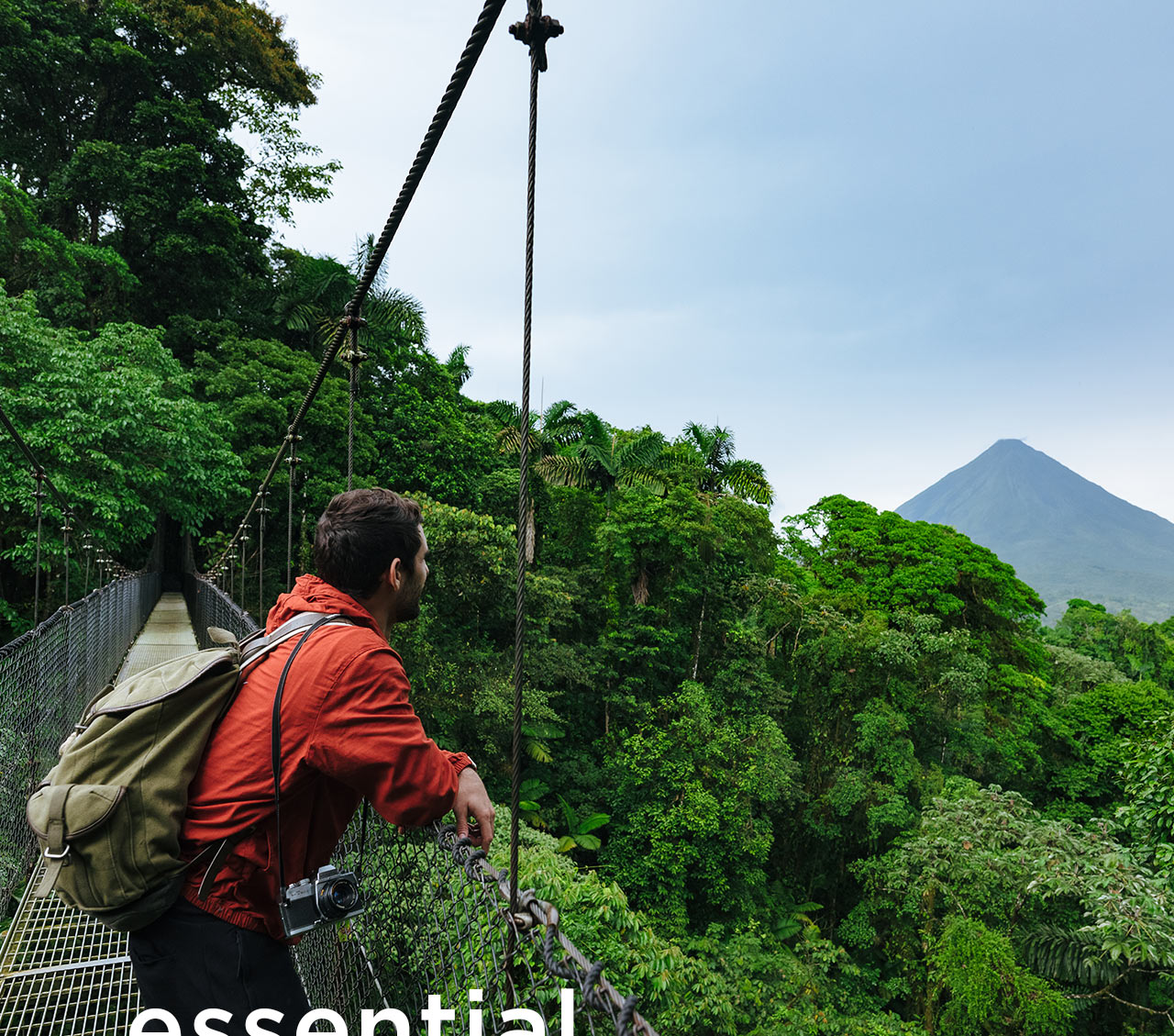 A man stands on a suspension footbridge overlooking a tropical forest. A headline reads: Essential Experiences.